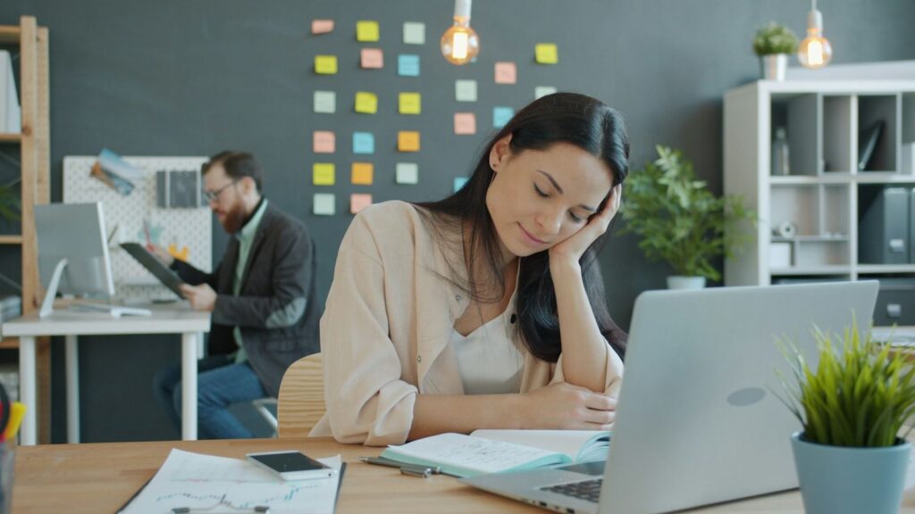 A woman resting her head on her hand at a desk in an office