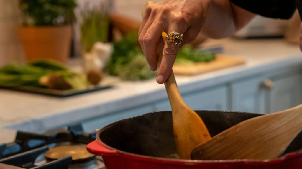 A hand stirring a pot with a wooden spoon on a home stove