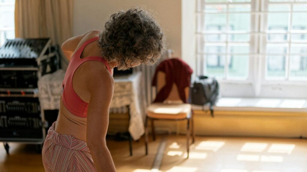 A woman with grey curly hair exercising in a sunlit room