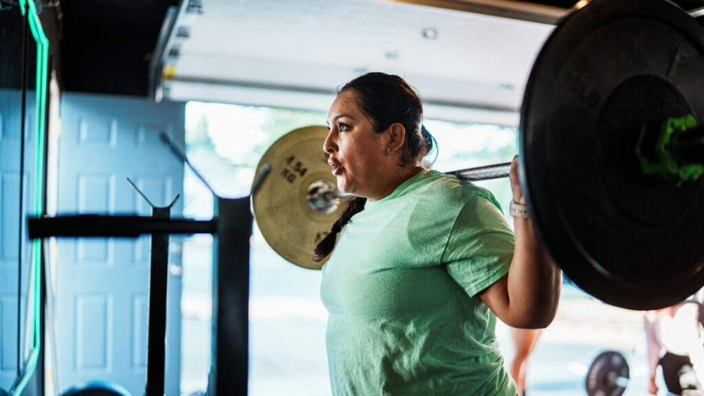A woman lifting a barbell overhead in a bright gym